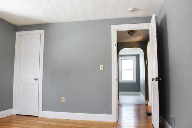 unfurnished room with light wood-style flooring, arched walkways, and baseboards