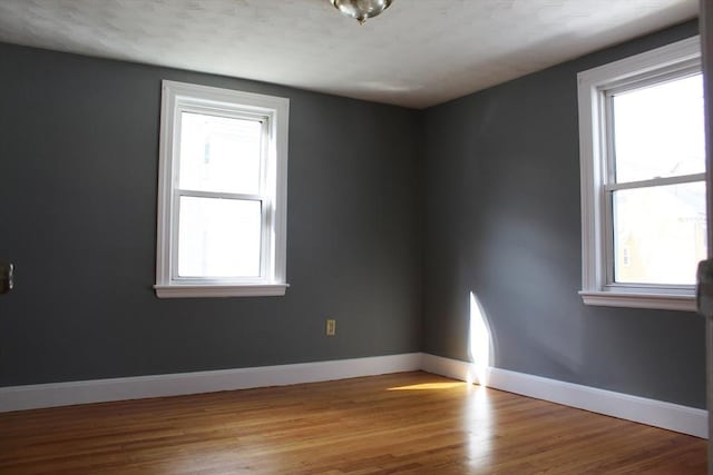 unfurnished room featuring a wealth of natural light, baseboards, and wood finished floors