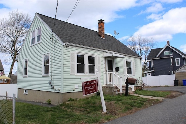 new england style home featuring fence, a shingled roof, and a chimney