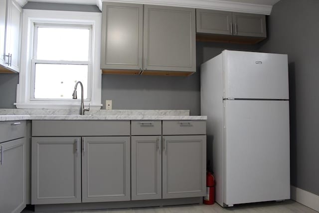 kitchen featuring gray cabinets, freestanding refrigerator, and a sink