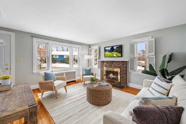 living room featuring plenty of natural light, radiator heating unit, light hardwood / wood-style floors, and a brick fireplace