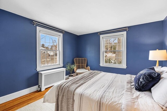 bedroom with multiple windows, wood-type flooring, and radiator heating unit