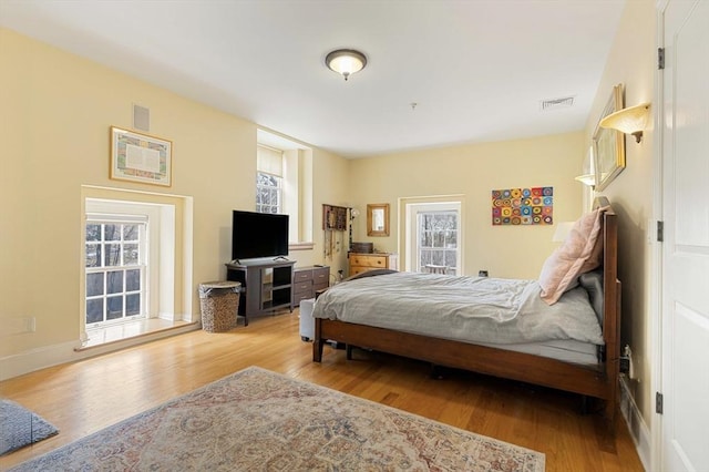 bedroom with baseboards, visible vents, and wood finished floors