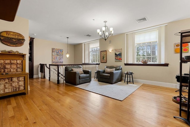 living area with baseboards, an inviting chandelier, visible vents, and light wood-style floors