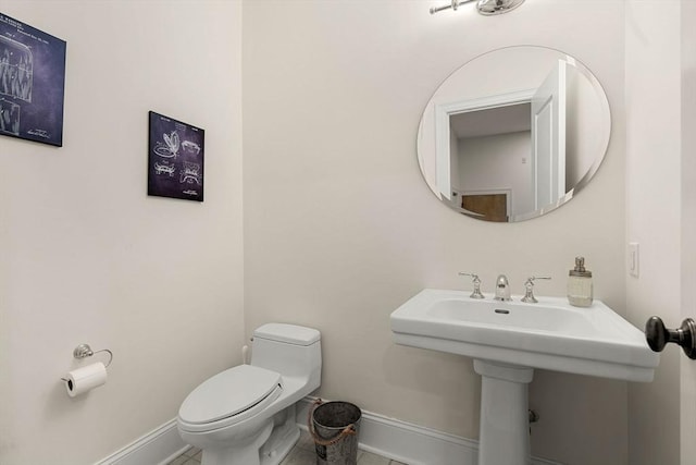 half bathroom featuring baseboards, a sink, tile patterned flooring, and toilet
