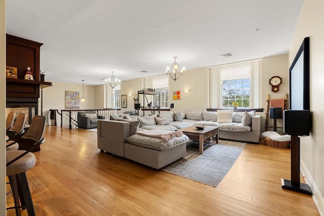living area featuring an inviting chandelier, light wood finished floors, visible vents, and a fireplace