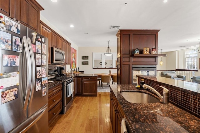 kitchen with a sink, light wood-style flooring, dark stone countertops, stainless steel appliances, and pendant lighting