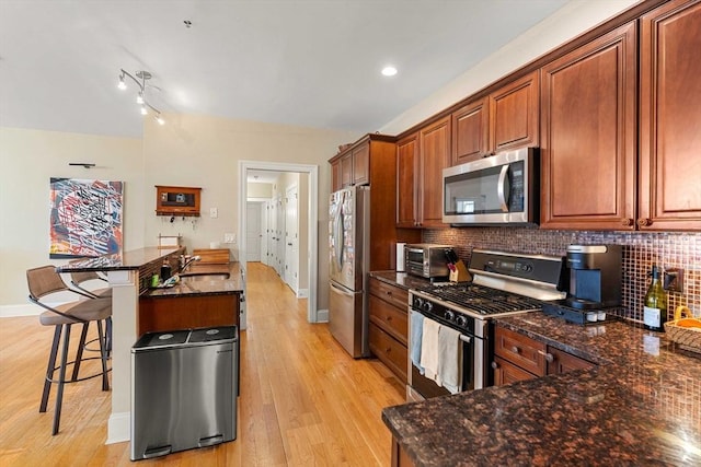 kitchen with a sink, a breakfast bar area, light wood-style flooring, stainless steel appliances, and backsplash