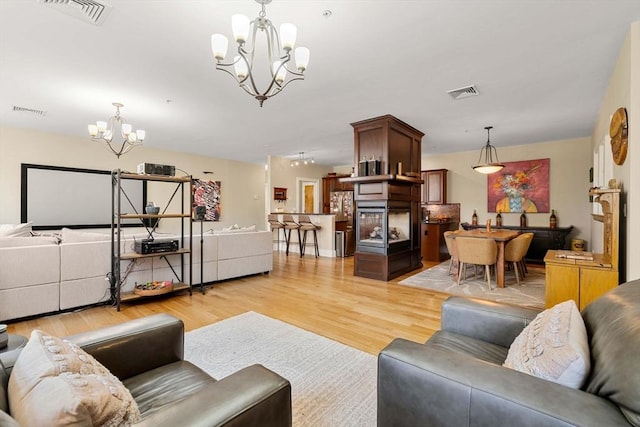 living room with an inviting chandelier, light wood-style floors, and visible vents