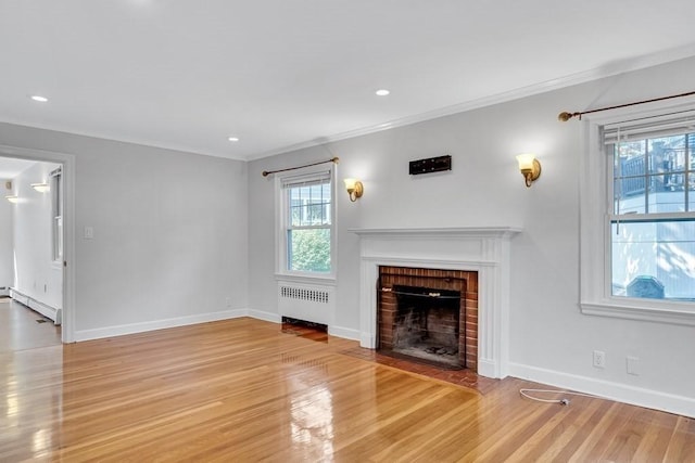 unfurnished living room featuring wood finished floors, baseboards, ornamental molding, a brick fireplace, and radiator