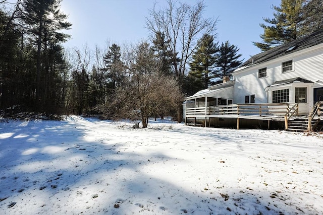 snowy yard featuring a sunroom and a deck