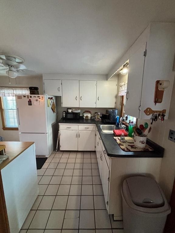 kitchen featuring dark countertops, freestanding refrigerator, white cabinetry, a sink, and light tile patterned flooring