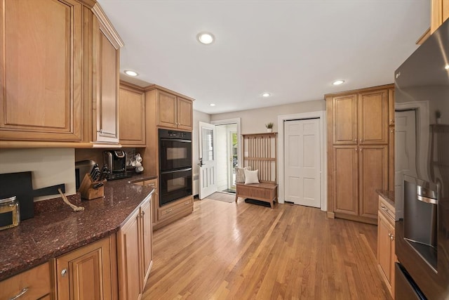 kitchen featuring dobule oven black, stainless steel fridge with ice dispenser, dark stone countertops, light wood-style floors, and recessed lighting