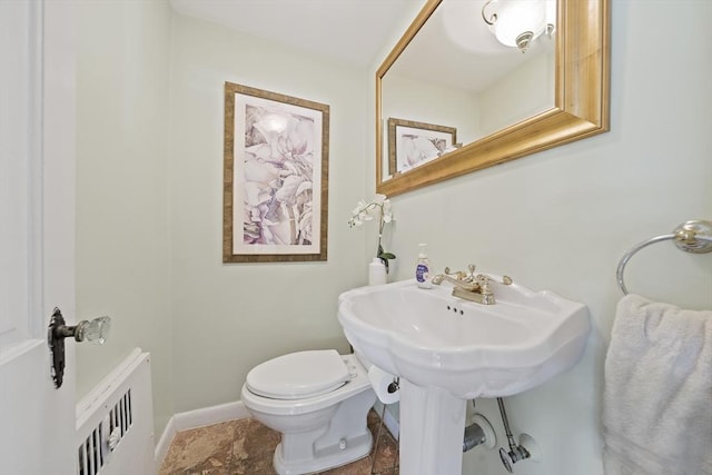 half bath featuring a sink, radiator, baseboards, and toilet