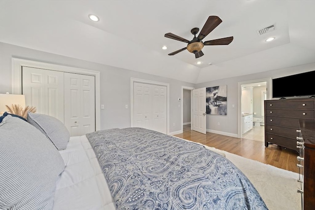 bedroom featuring visible vents, lofted ceiling, two closets, wood finished floors, and a ceiling fan