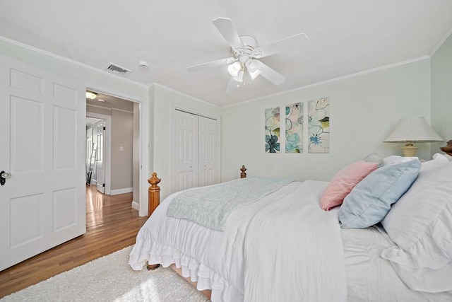 bedroom featuring visible vents, crown molding, a closet, wood finished floors, and baseboards