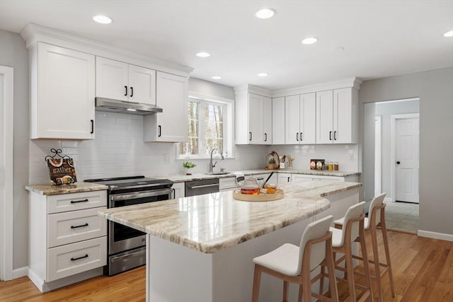 kitchen with under cabinet range hood, appliances with stainless steel finishes, a breakfast bar area, and white cabinets