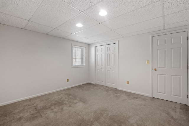 unfurnished bedroom with a drop ceiling, a closet, baseboards, and carpet