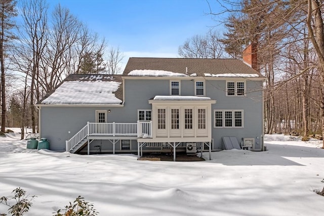 snow covered back of property featuring stairway, a chimney, and a deck