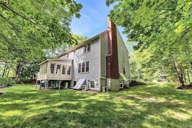 back of property with a lawn, a sunroom, and a chimney