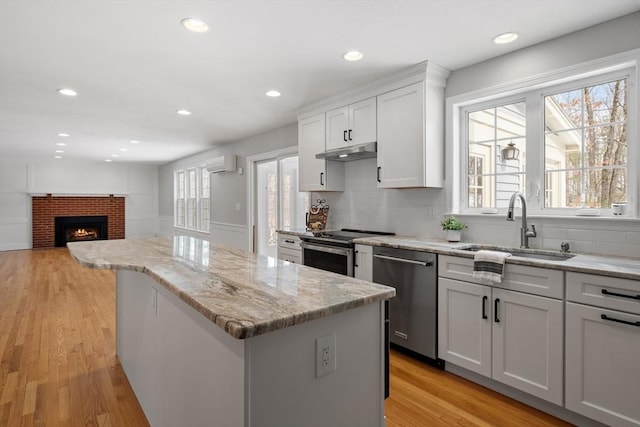 kitchen featuring under cabinet range hood, a sink, a center island, stainless steel appliances, and a brick fireplace