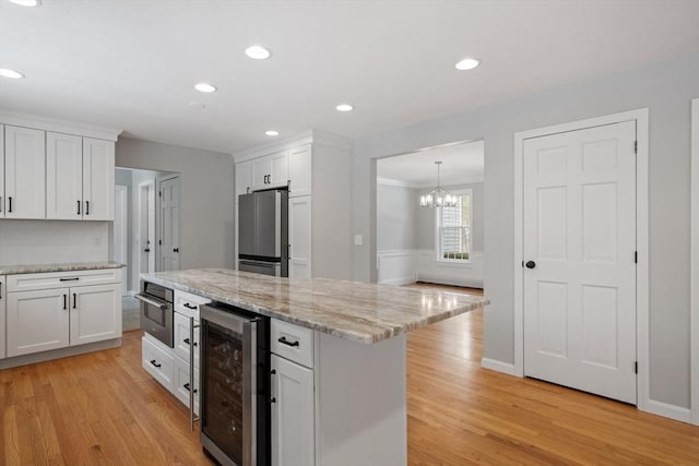 kitchen featuring light wood-type flooring, stainless steel appliances, wine cooler, and white cabinetry