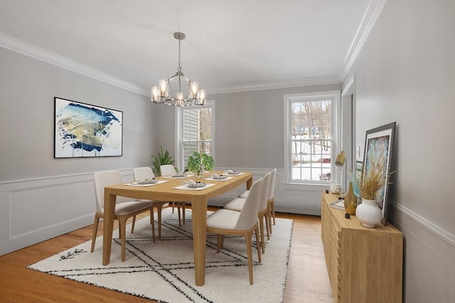 dining room featuring wainscoting, crown molding, a decorative wall, a notable chandelier, and light wood-type flooring