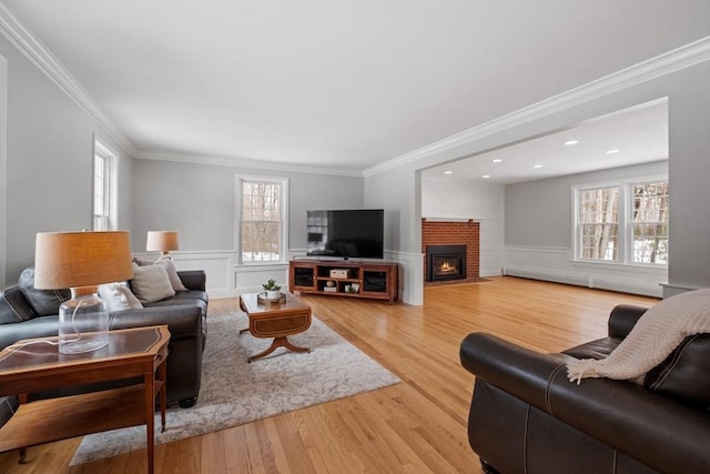 living room with a brick fireplace, a healthy amount of sunlight, light wood-style flooring, and wainscoting