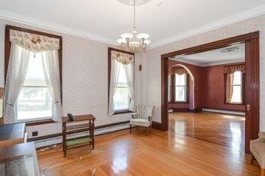 unfurnished room featuring wood-type flooring, ornamental molding, baseboard heating, and a chandelier