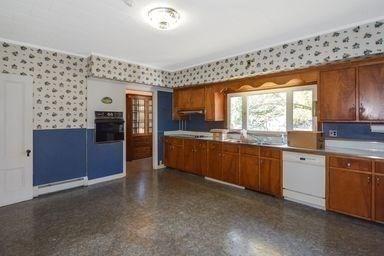 32 Mount Pleasant St, North Brookfield, MA 01535 - kitchen featuring wallpapered walls, black oven, brown cabinetry, white dishwasher, and a sink