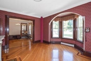 interior space featuring hardwood / wood-style flooring, crown molding, baseboard heating, and a chandelier