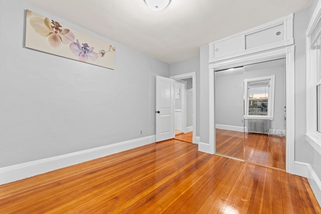 unfurnished bedroom with a closet, radiator heating unit, and hardwood / wood-style floors