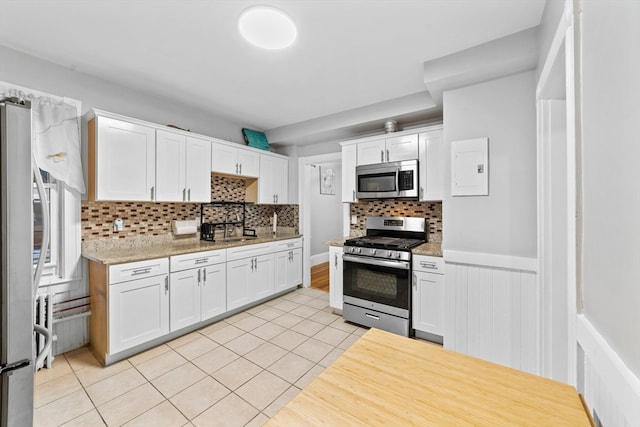 kitchen with white cabinets, appliances with stainless steel finishes, light tile patterned flooring, and tasteful backsplash