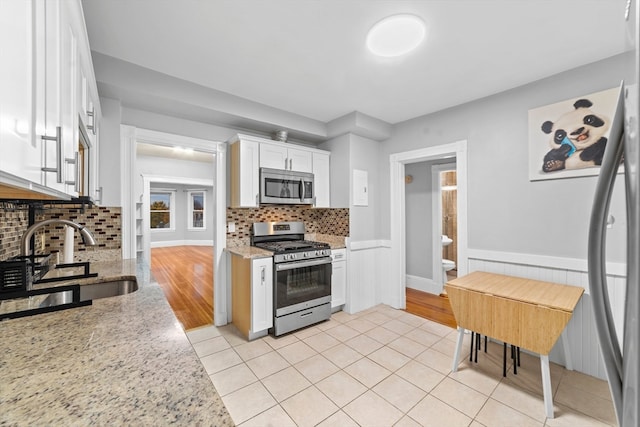 kitchen with light stone counters, stainless steel appliances, backsplash, white cabinetry, and sink