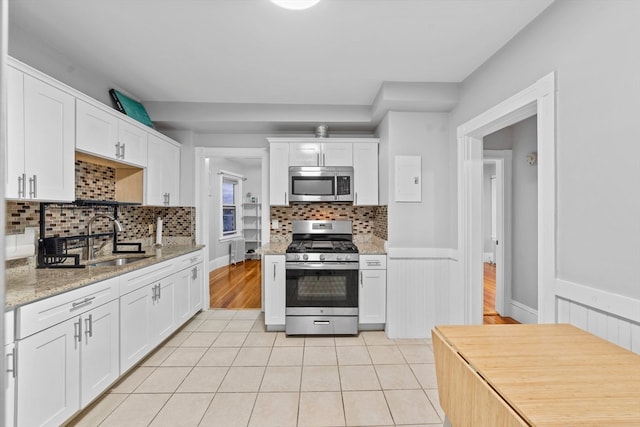 kitchen with stainless steel appliances, sink, light stone counters, tasteful backsplash, and white cabinets