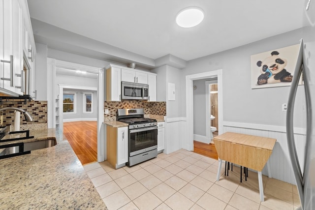 kitchen with sink, appliances with stainless steel finishes, light stone countertops, backsplash, and white cabinets