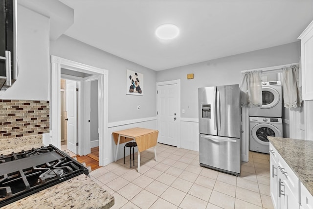 kitchen with stacked washer and clothes dryer, white cabinetry, light stone counters, tasteful backsplash, and stainless steel fridge