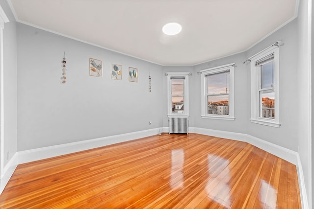 empty room with hardwood / wood-style floors, radiator heating unit, and crown molding