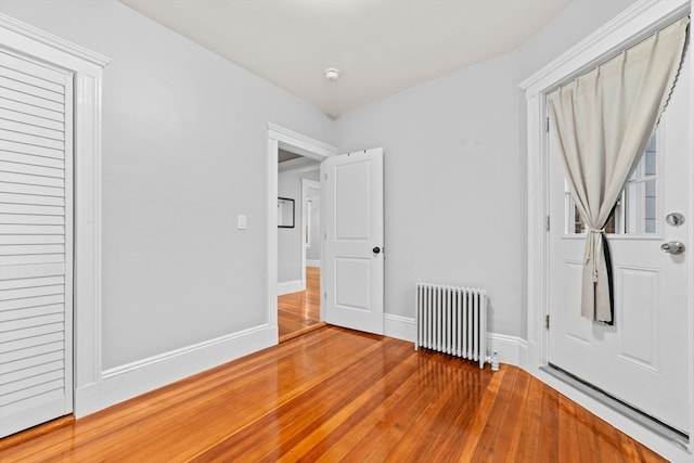 unfurnished bedroom with hardwood / wood-style floors, radiator, and a closet