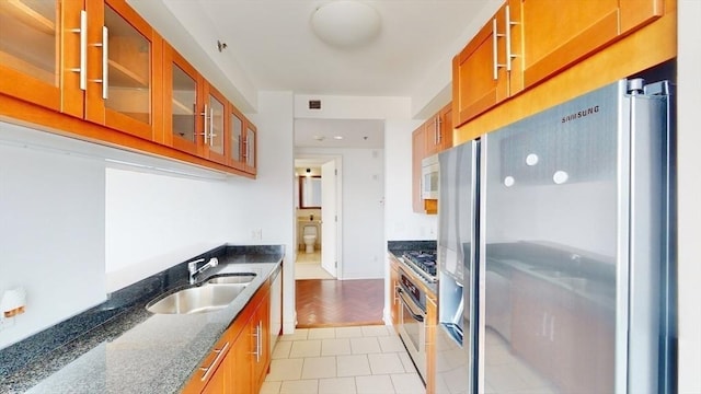 kitchen with dark stone countertops, sink, light tile patterned floors, and appliances with stainless steel finishes