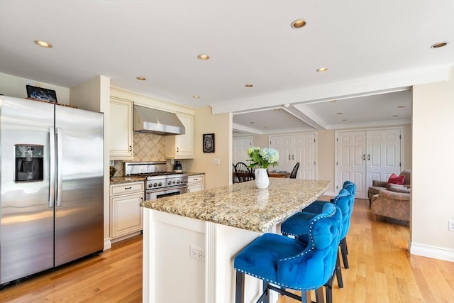 kitchen featuring a breakfast bar, appliances with stainless steel finishes, light stone countertops, a kitchen island, and wall chimney exhaust hood