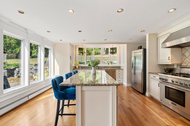 kitchen with baseboard heating, appliances with stainless steel finishes, a kitchen island, light stone countertops, and light hardwood / wood-style floors