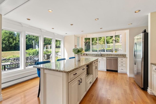 kitchen featuring a kitchen bar, light stone counters, a center island, a baseboard radiator, and stainless steel appliances