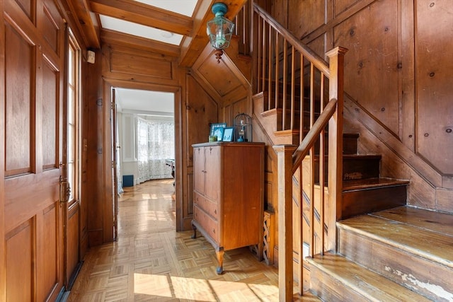 stairway featuring a skylight, wooden walls, beamed ceiling, and parquet flooring