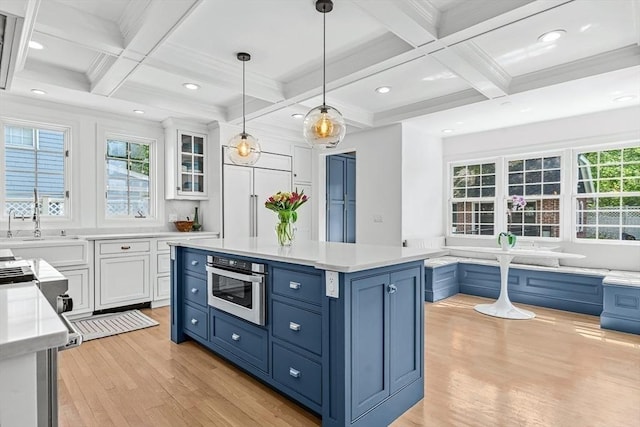 kitchen featuring blue cabinets, light wood-style flooring, coffered ceiling, white cabinets, and oven