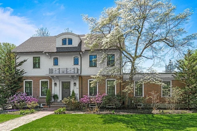 view of front of home with a front lawn, brick siding, and a balcony