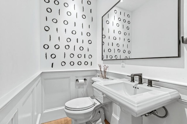 bathroom featuring a wainscoted wall, toilet, a decorative wall, a sink, and wood finished floors