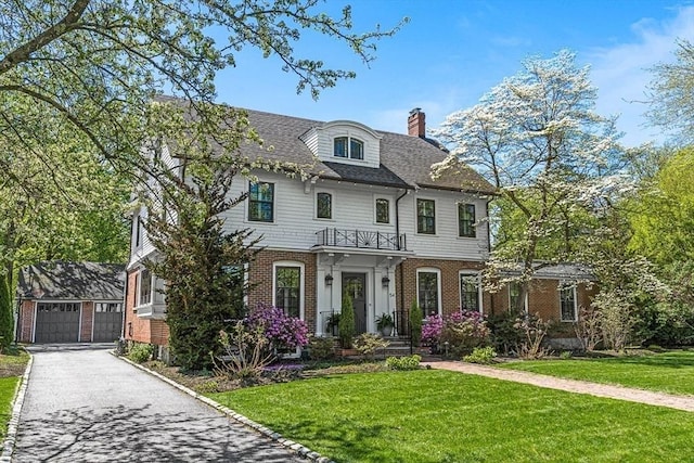 view of front of home with brick siding, a chimney, a front lawn, and a detached garage