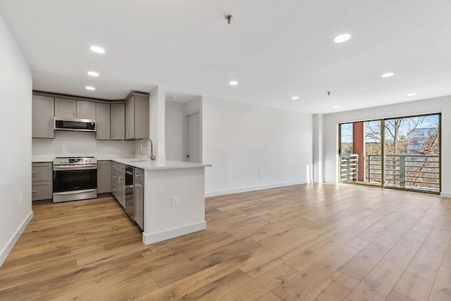 kitchen featuring sink, light hardwood / wood-style flooring, gray cabinets, stainless steel appliances, and kitchen peninsula