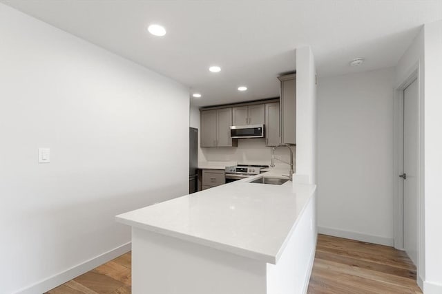 kitchen featuring sink, gray cabinetry, kitchen peninsula, stainless steel appliances, and light hardwood / wood-style floors